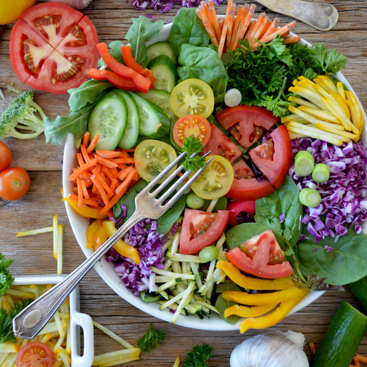 This is an image of a plate full of colorful sliced vegetables and fruit with a fork on a picnic table-like background..